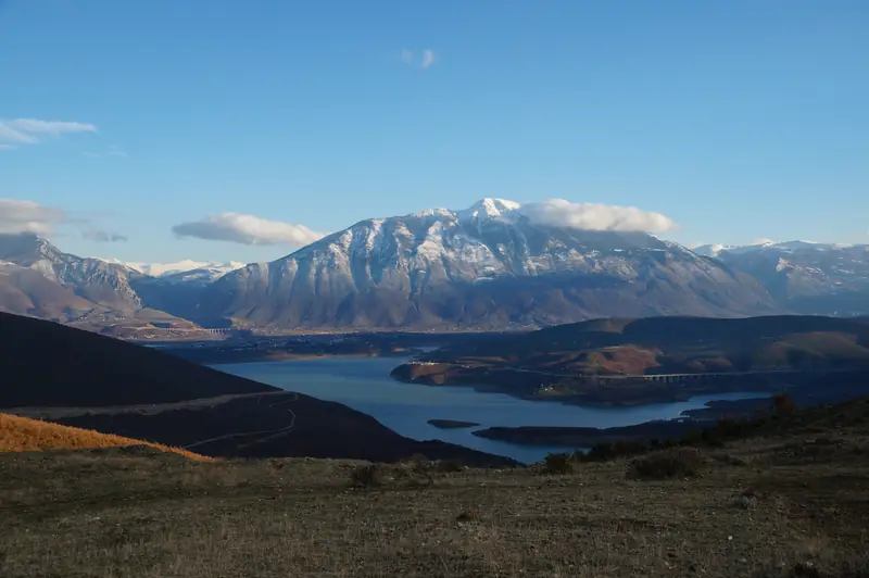 A long reservoir lake between steep green hills with a mountain behind