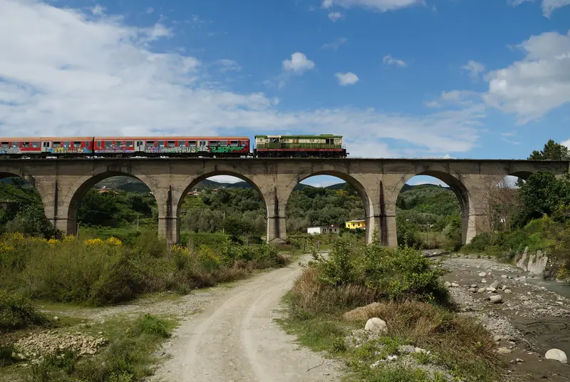 A passenger train crossing an arched stone railway bridge in Albania